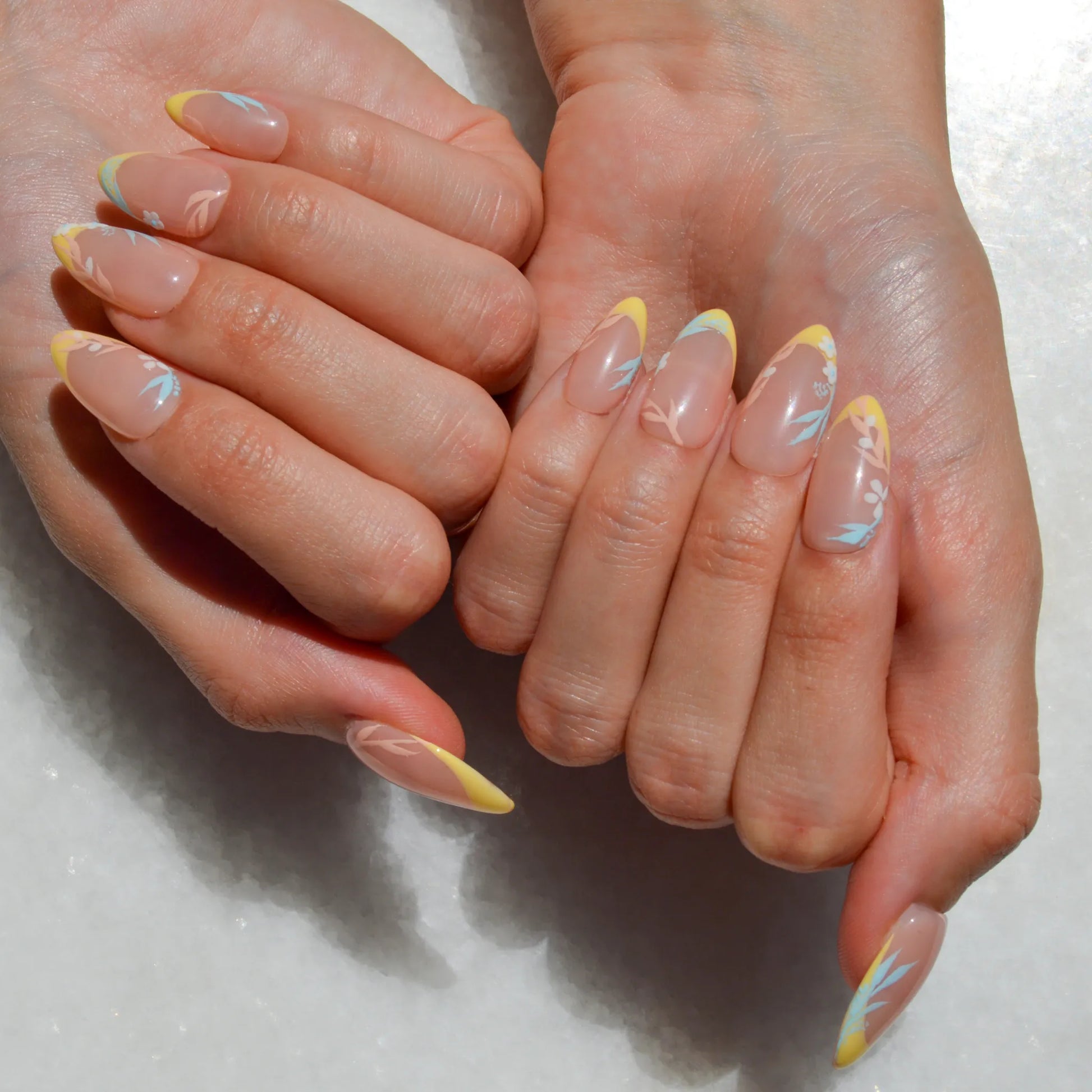 Manucure press-on Secret Garden portée, aux tons nude et jaune pastel avec détails floraux bleus et blancs.