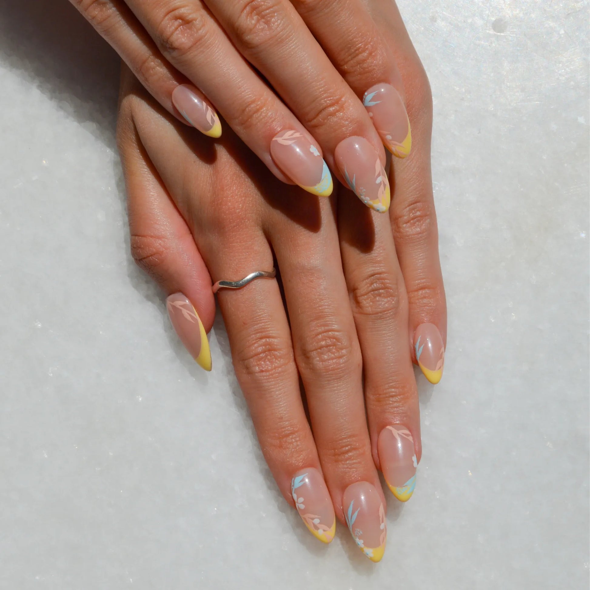 Mains portant les faux ongles Secret Garden en extérieur, mettant en valeur les tons nude et jaunes sous la lumière naturelle.