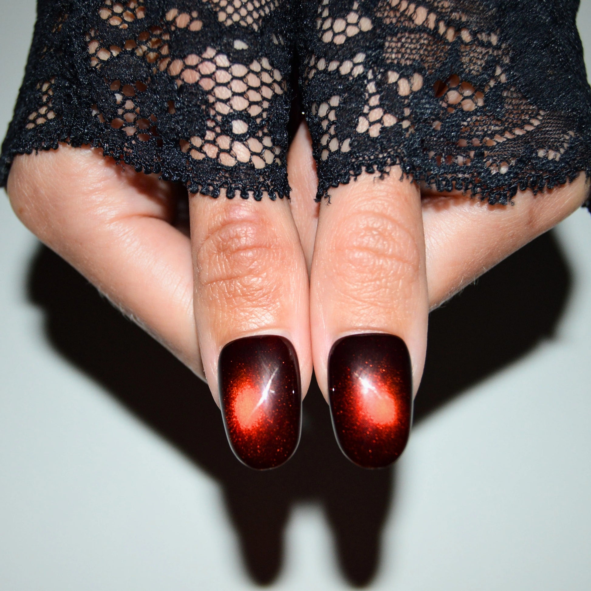 Set de press-on nails faits main en gel et acrylique, design cat eye rouge intense sur ongles ovales, présenté sur deux pouces.