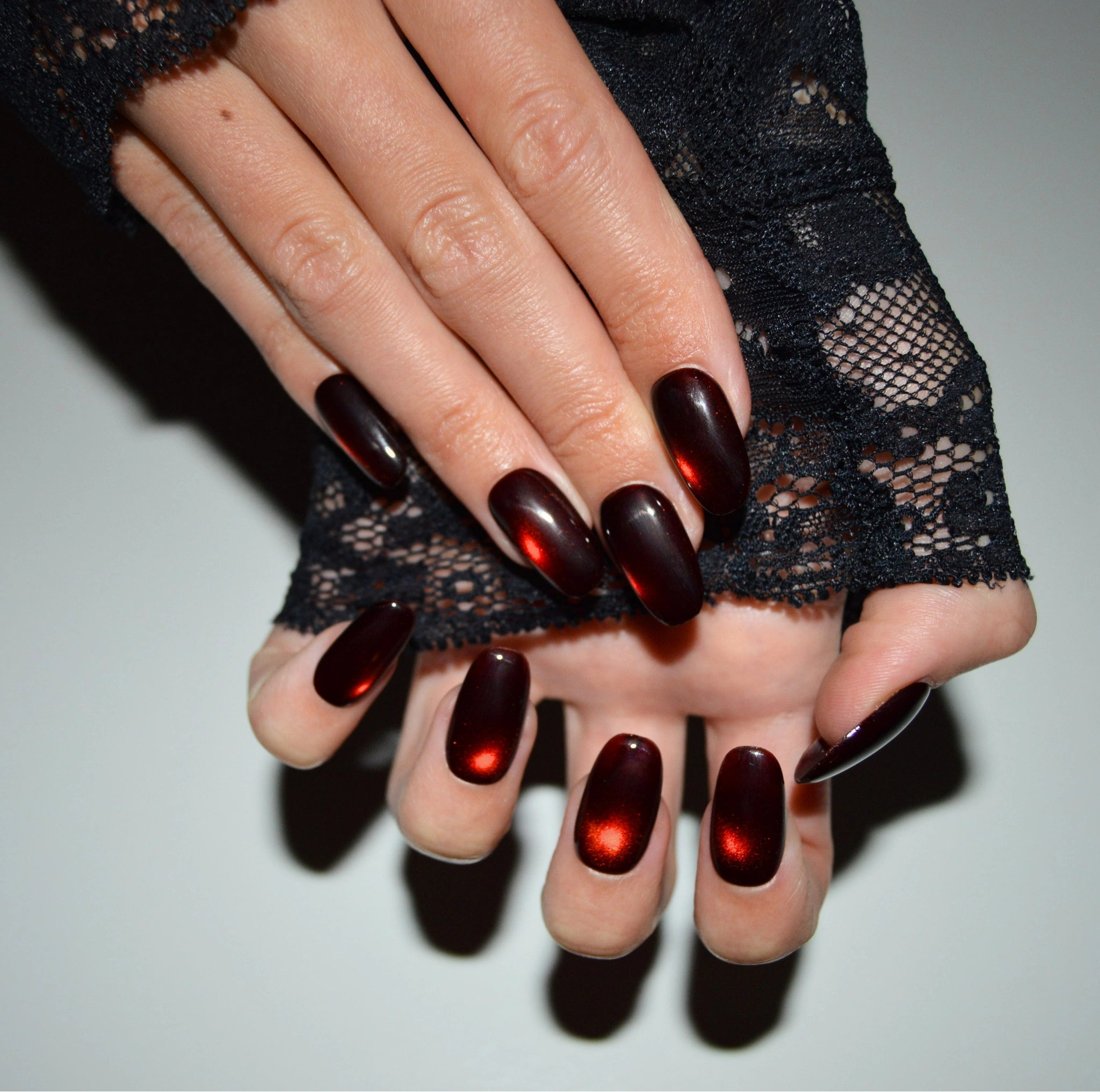 Manucure press-on handmade avec finition gel et acrylique, dégradé cat eye rouge foncé, mains posées l’une sur l’autre.