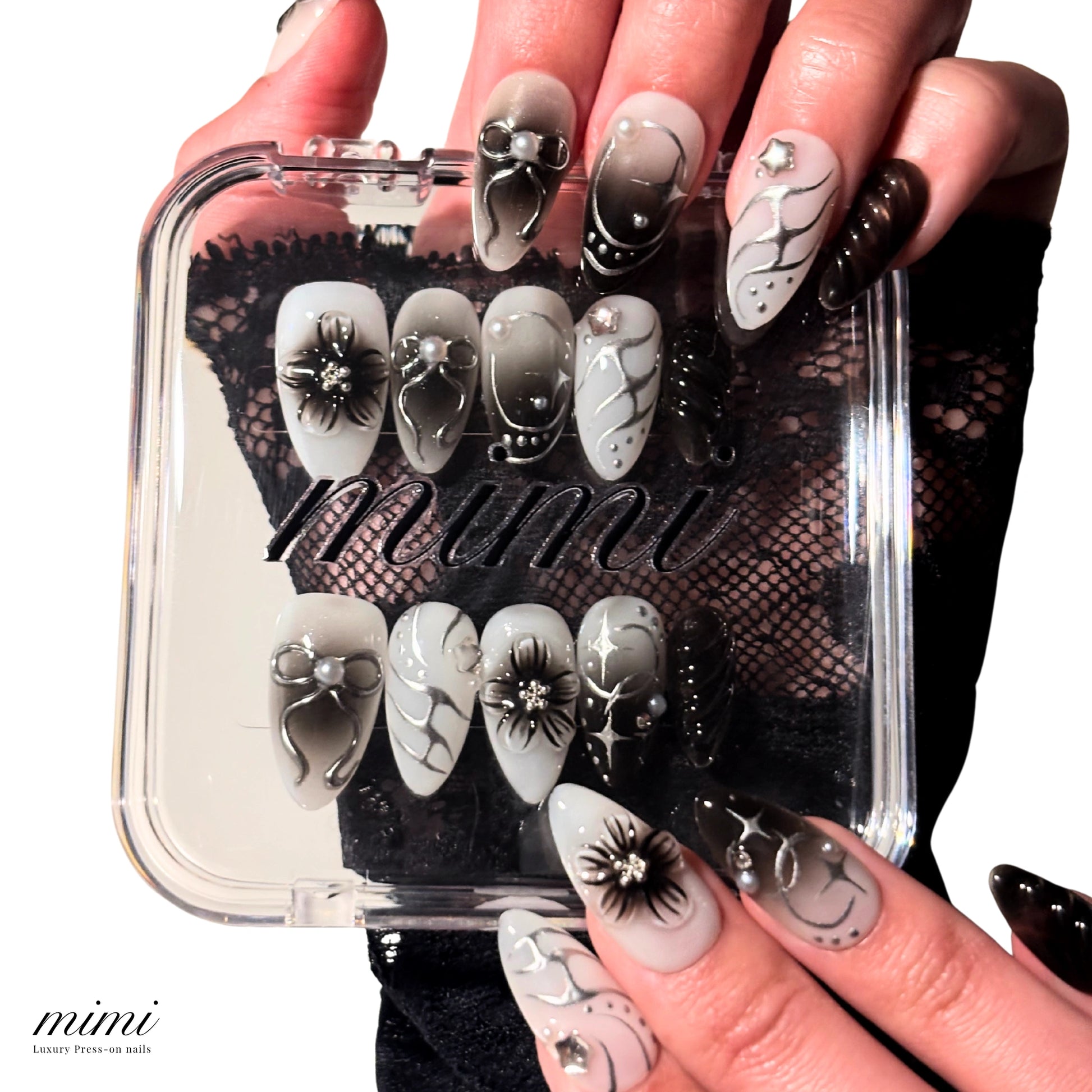 Mains portant les press-on nails Shadow Petal faits main en gel et acrylique, design noir et blanc 3D avec fleurs et nœuds, présentation avec la boîte Mimi.